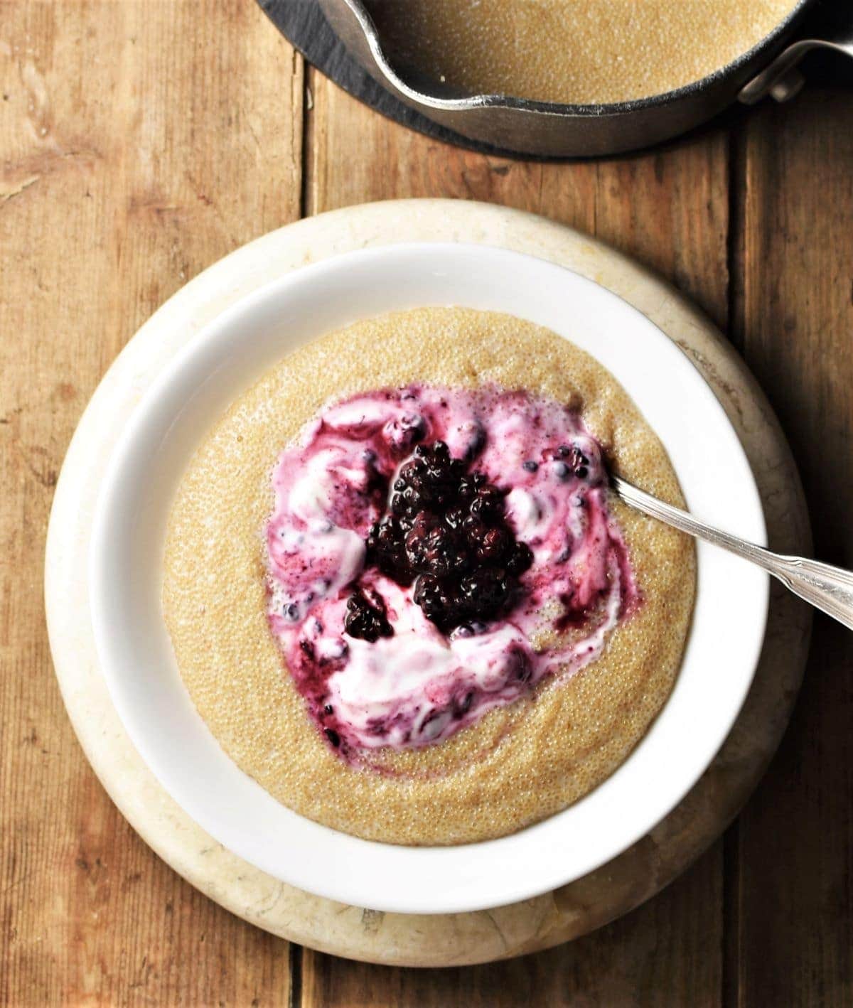 Top down view of amaranth porridge with fruit and yogurt in white bowl with spoon.