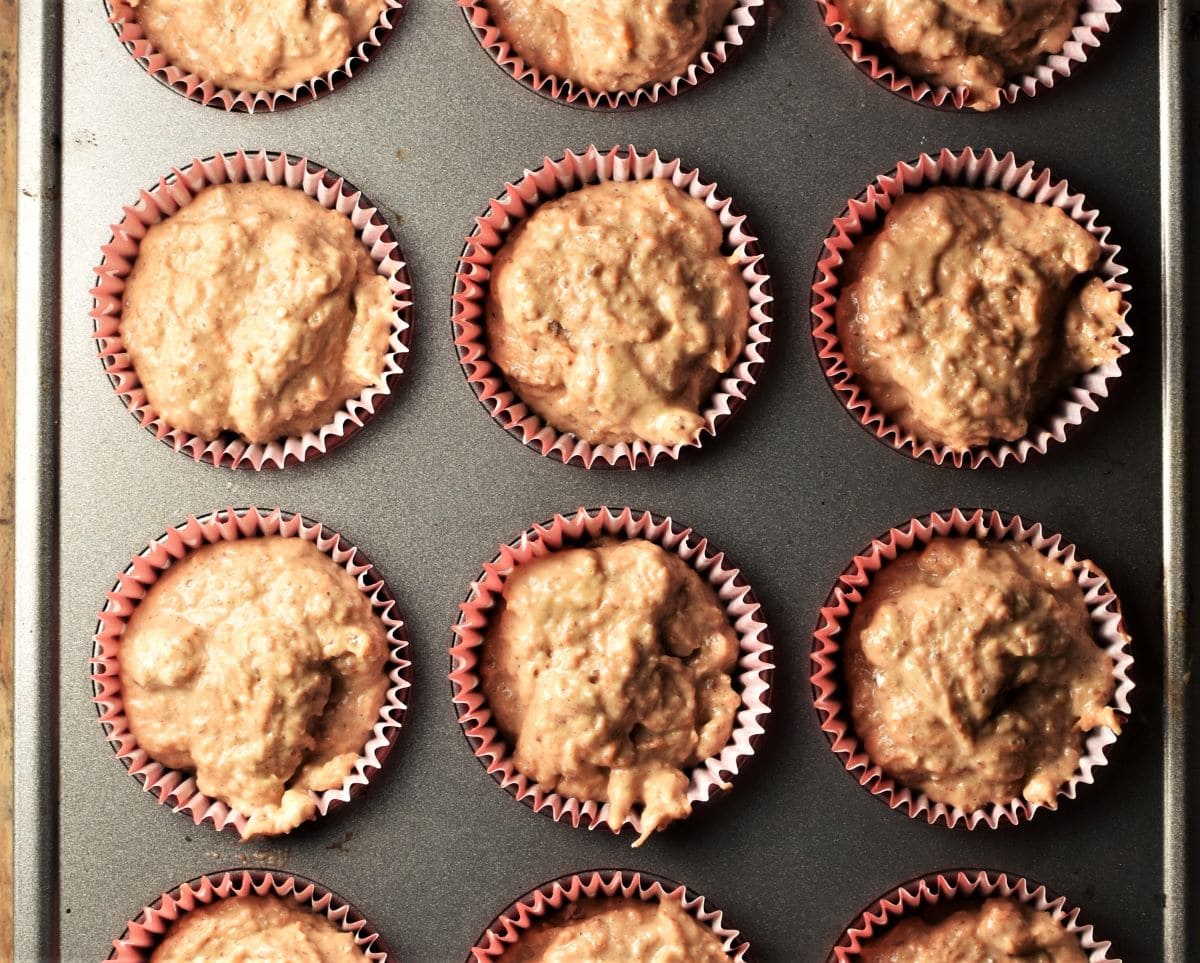 Unbaked carrot muffins in red liners in pan.