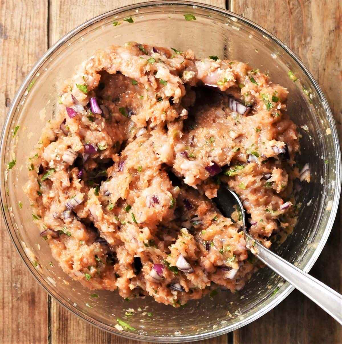 Chicken burgers mixture with spoon in mixing bowl.