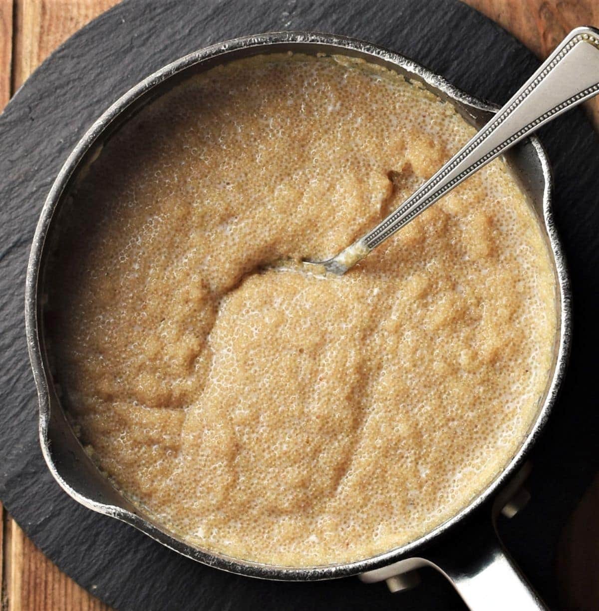 Thick amaranth porridge with spoon in saucepan.