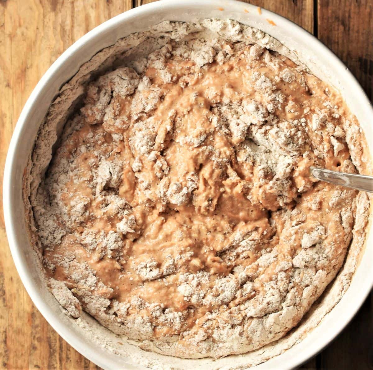 Carrot muffins batter in white bowl with some flour visible.