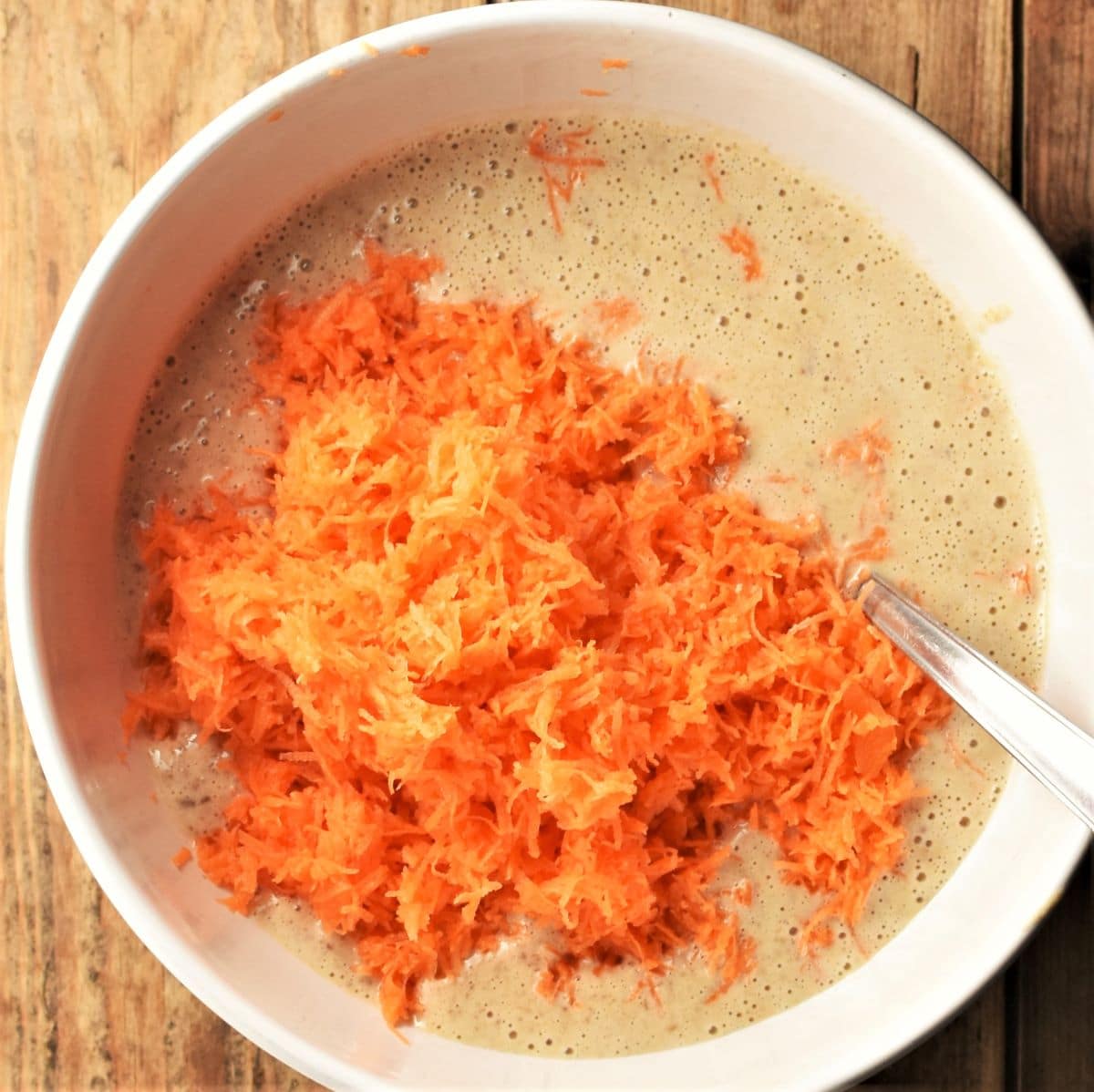 Grated carrot with muffin batter in white bowl with spoon.