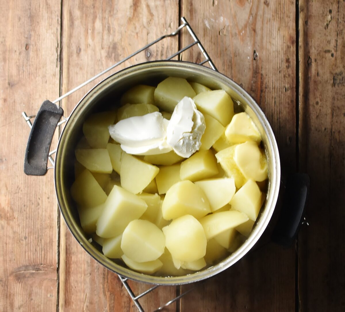 Peeled potato pieces with butter and cream cheese in pot.