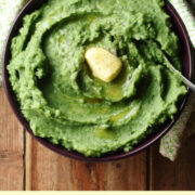Top down view of spinach mashed potatoes in bowl with spoon and knob of butter.