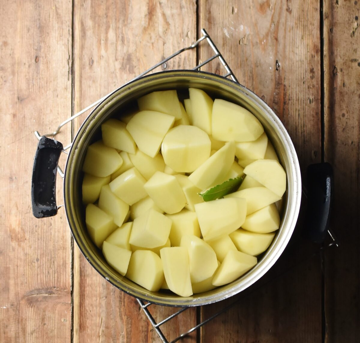 Peeled potato pieces with bay leaf in pot with water.
