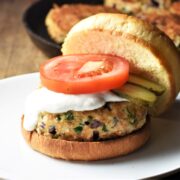 Chicken burger in open bun with sauce, slice of tomato and pickles.