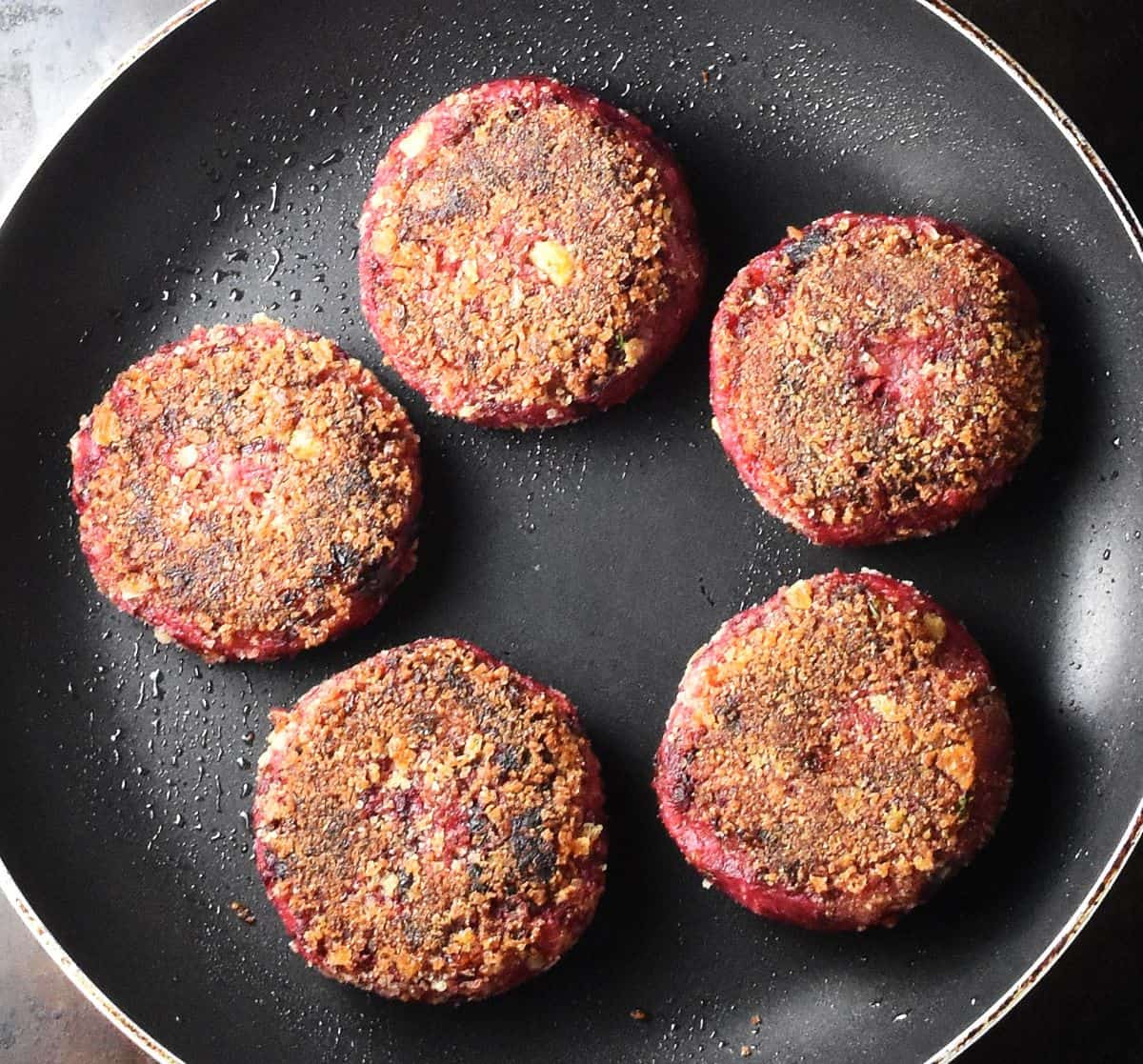 Top down view of 5 cooked, browned beet patties in pan.