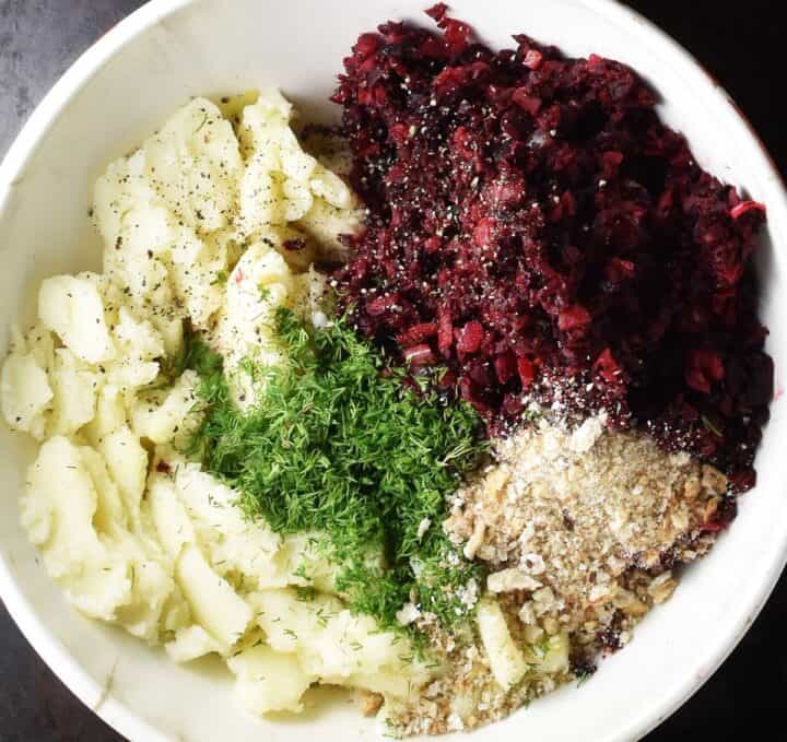 Mashed potato with beetroot mixture, breadcrumbs and dill in white bowl.