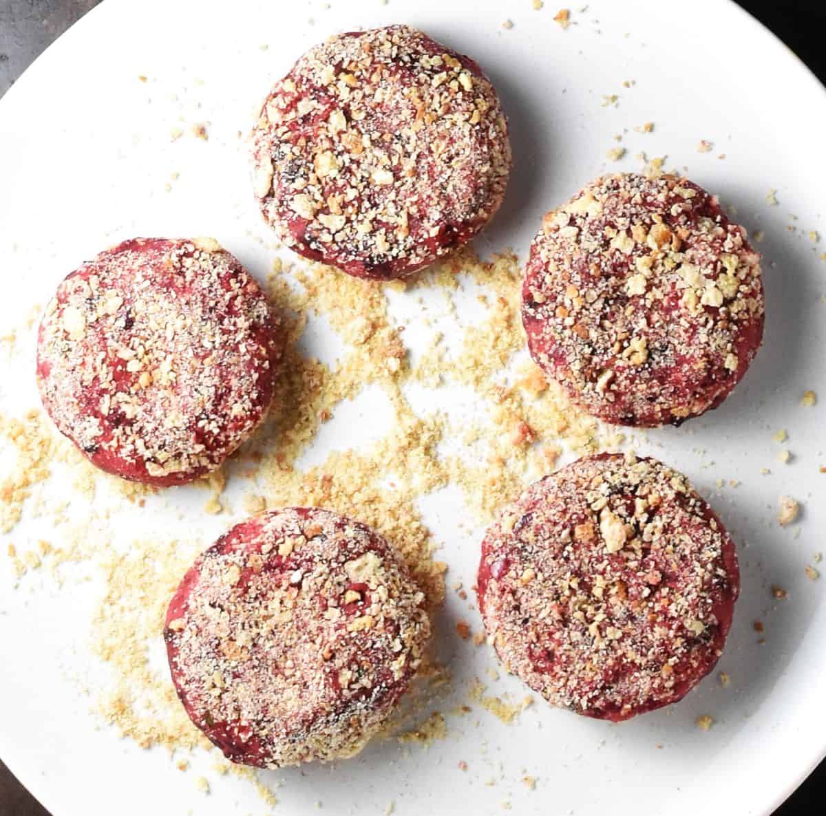 5 breaded beet potato cakes on white plate with breadcrumbs.