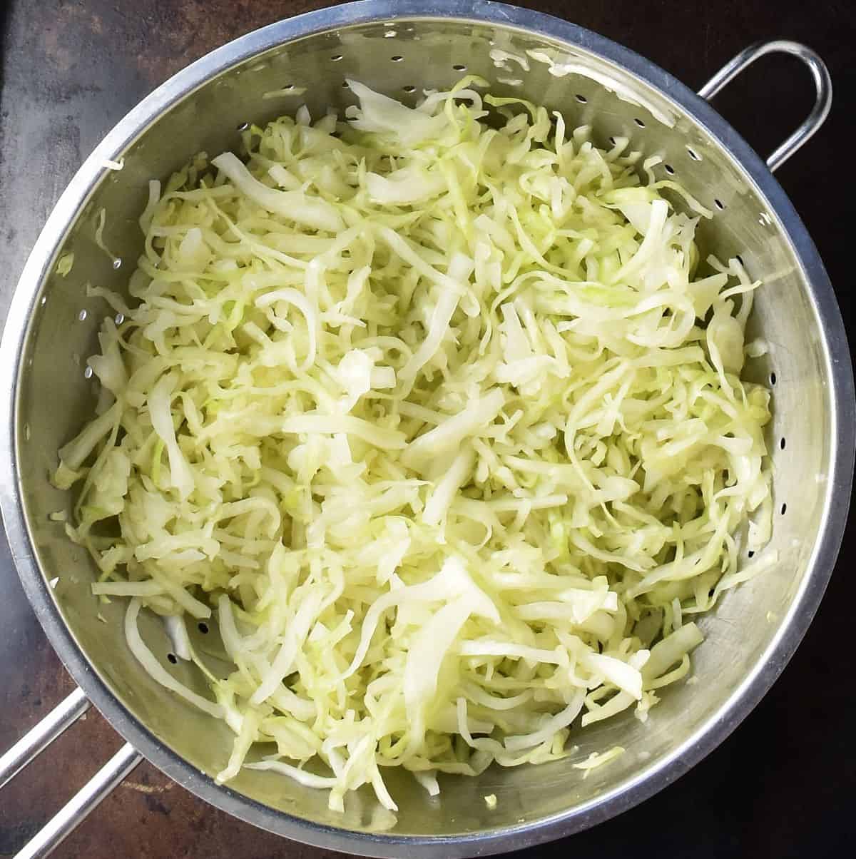 Top down view of shredded cabbage for Polish coleslaw in metal strainer.