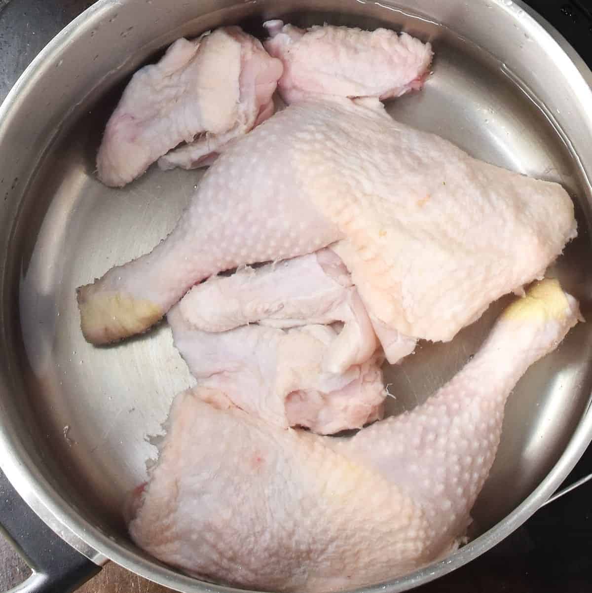 Top down view of chicken pieces in large metal pot with water.