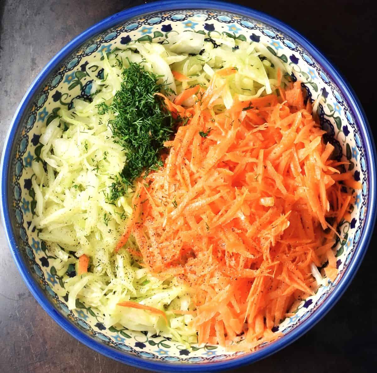 Top down view of shredded cabbage and carrot and chopped dill in Polish ceramic blue Boleslawiec bowl.