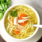 Top down view of Polish chicken noodle soup, rosół, in white bowl with spoon and fresh parsley in background.