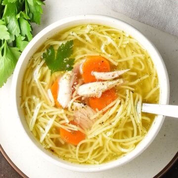 Top down view of Polish chicken noodle soup, rosół, in white bowl with spoon and fresh parsley in background.