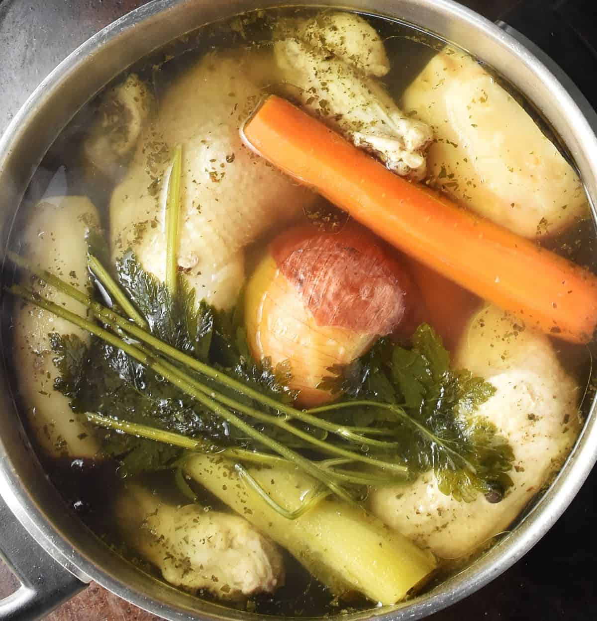 Top down view of Polish rosol soup with vegetables, herbs and chicken pieces at the top in large pot.