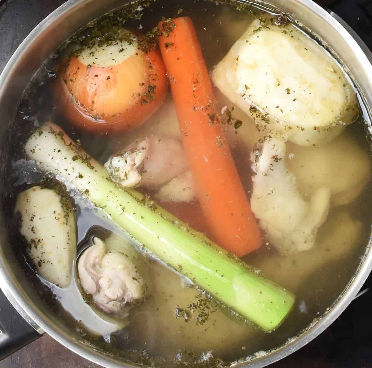 Top down view of rosol soup vegetables and chicken in large pot with water.