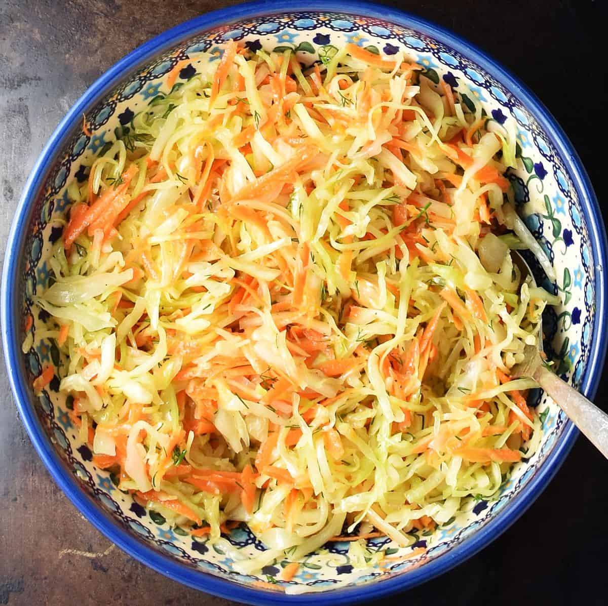 Assembled Polish cabbage coleslaw in large, blue Boleslawiec bowl with spoon.