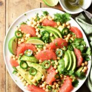 Grapefruit, avocado and chickpea salad on large plate with dressing in top right corner.