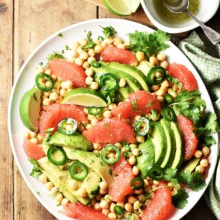 Grapefruit, avocado and chickpea salad on large plate with dressing in top right corner.