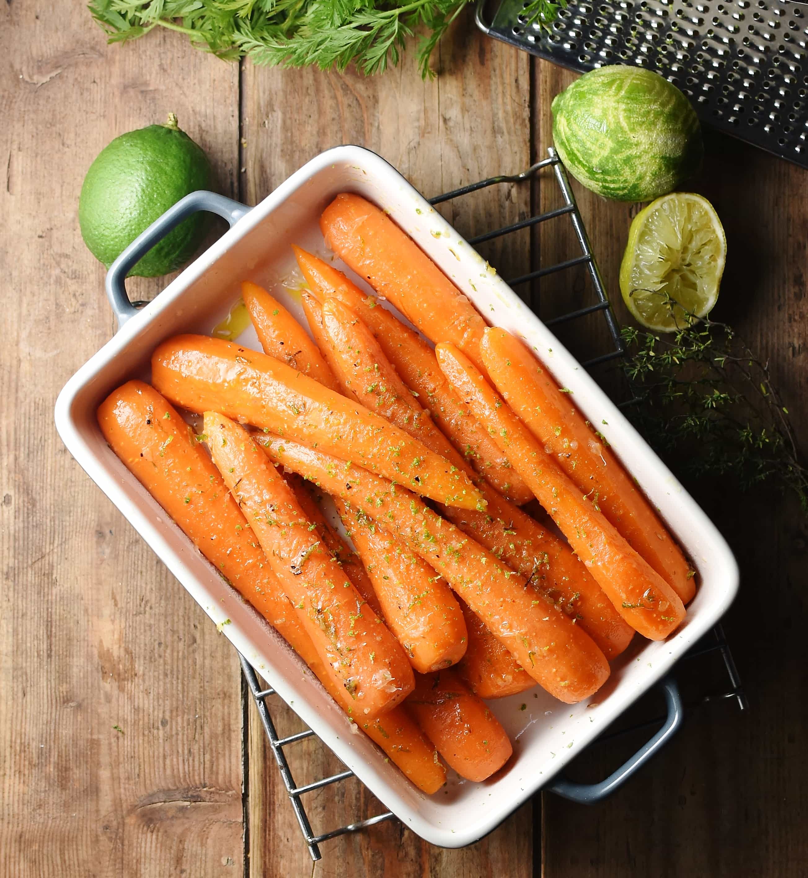 Top down view of braised carrots in white rectangular dish, with limes in background.