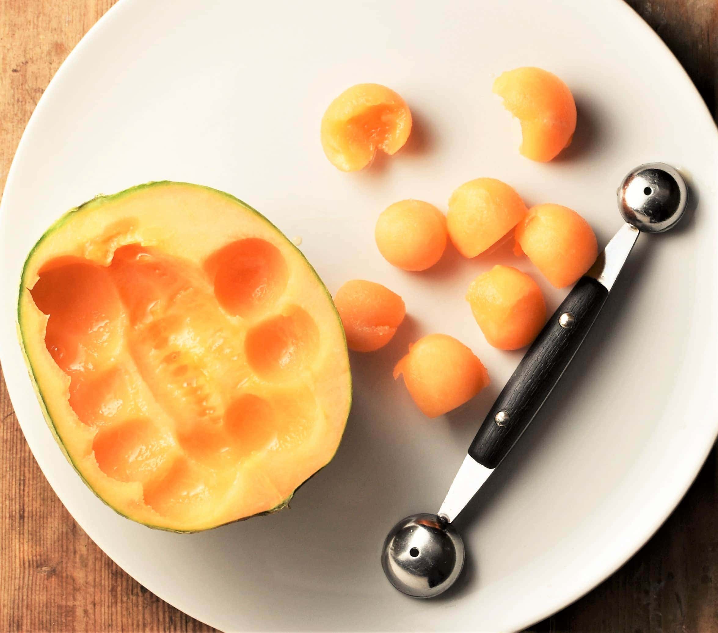 Halved cantaloupe with melon baller on white plate.
