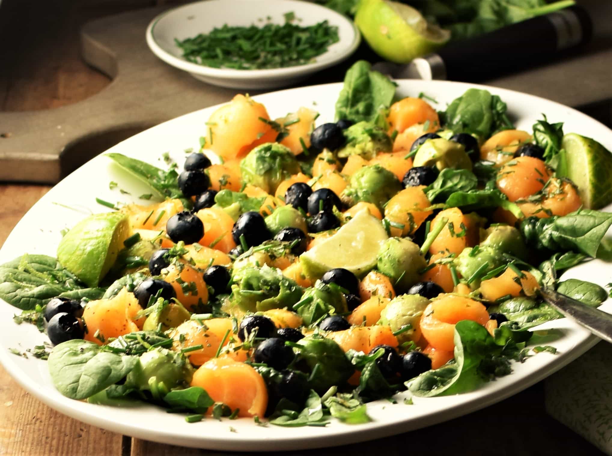 Side view of cantaloupe, spinach, blueberry and avocado salad on white plate.