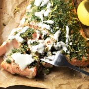 Close-up view of salmon with herbs and creamy sauce on top of parchment.