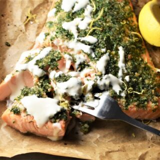 Close-up view of salmon with herbs and creamy sauce on top of parchment.