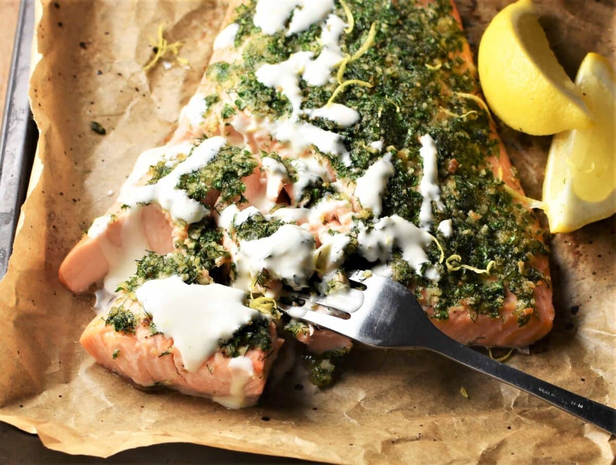 Close-up view of salmon with herbs and creamy sauce on top of parchment.