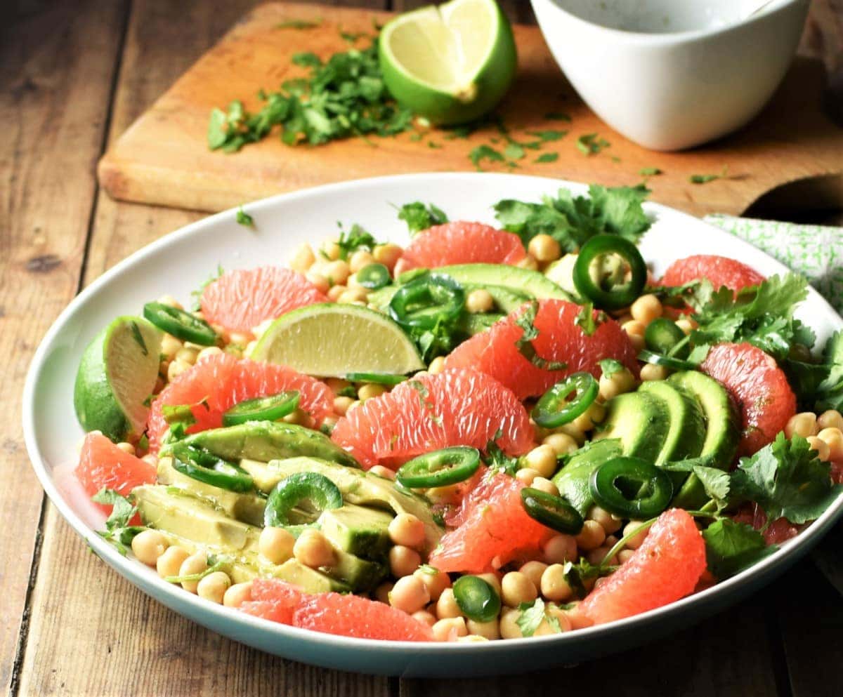 Side view of avocado grapefruit salad with chickpeas on large plate with lime in background.