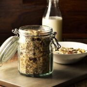 Homemade muesli in open jar, with bottle of milk and muesli in bowl in background.