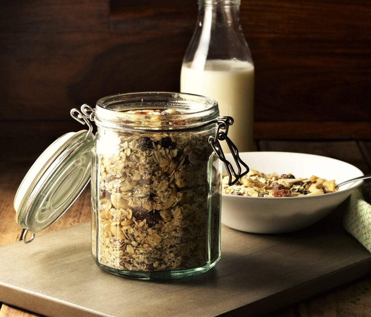 Homemade muesli in open jar, with bottle of milk and muesli in bowl in background.