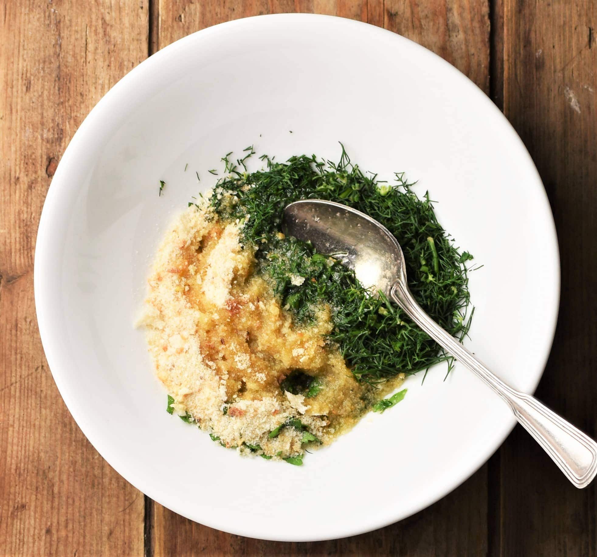 Chopped hers and breadcrumbs in white bowl with spoon.