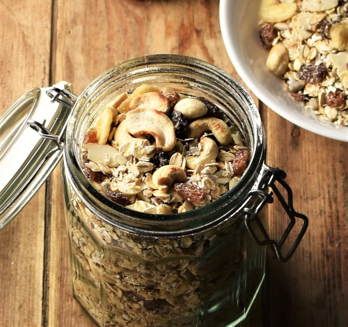 Close-up view of muesli in open jar with muesli in bowl in top right corner.