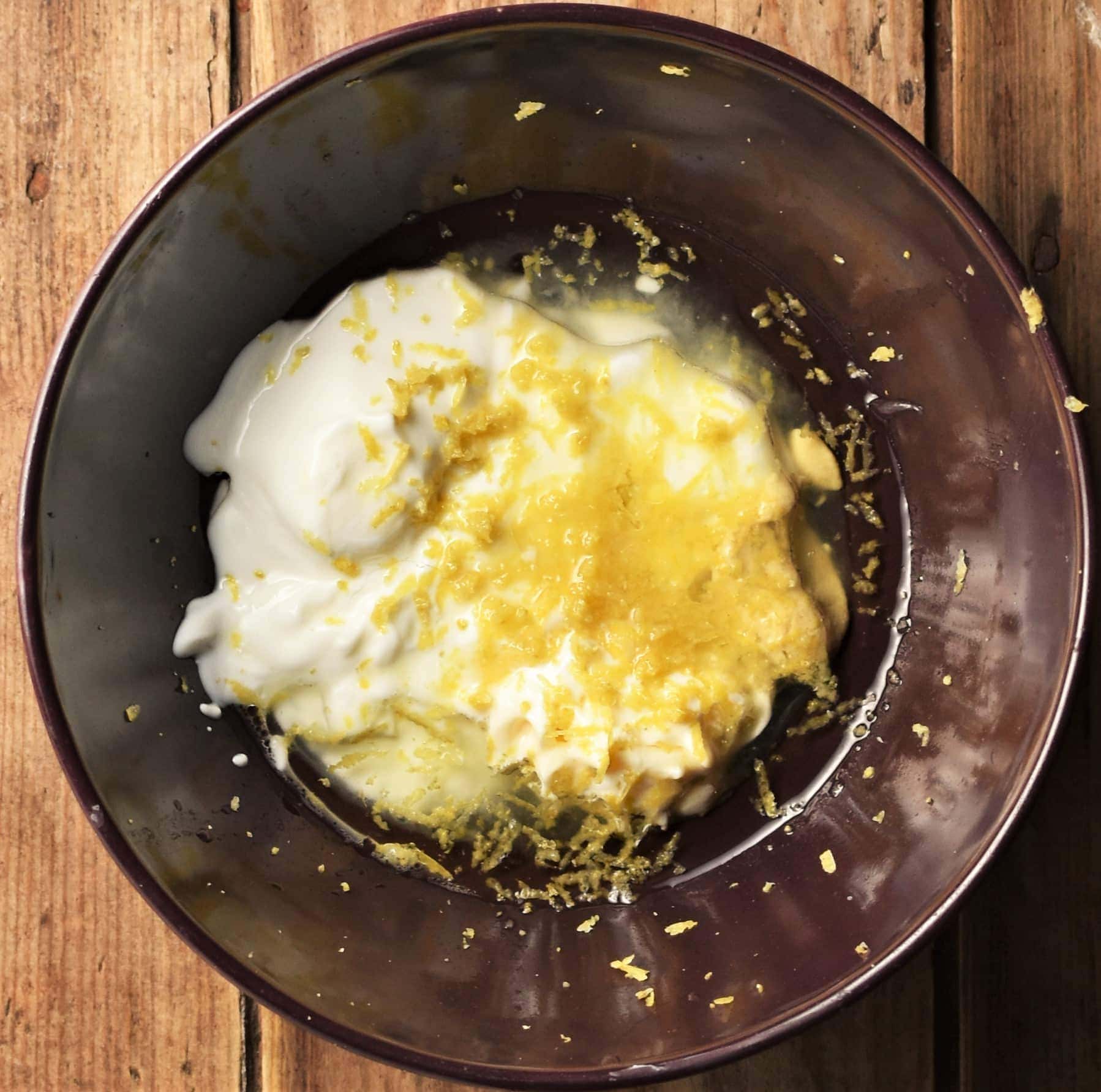 Yogurt, oil and lemon zest mixture in purple bowl.
