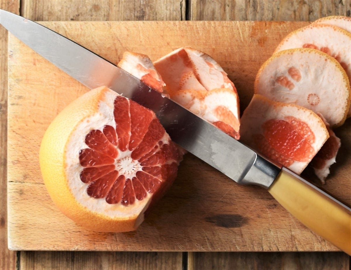 Peeling grapefruit on top of wooden board with knife.