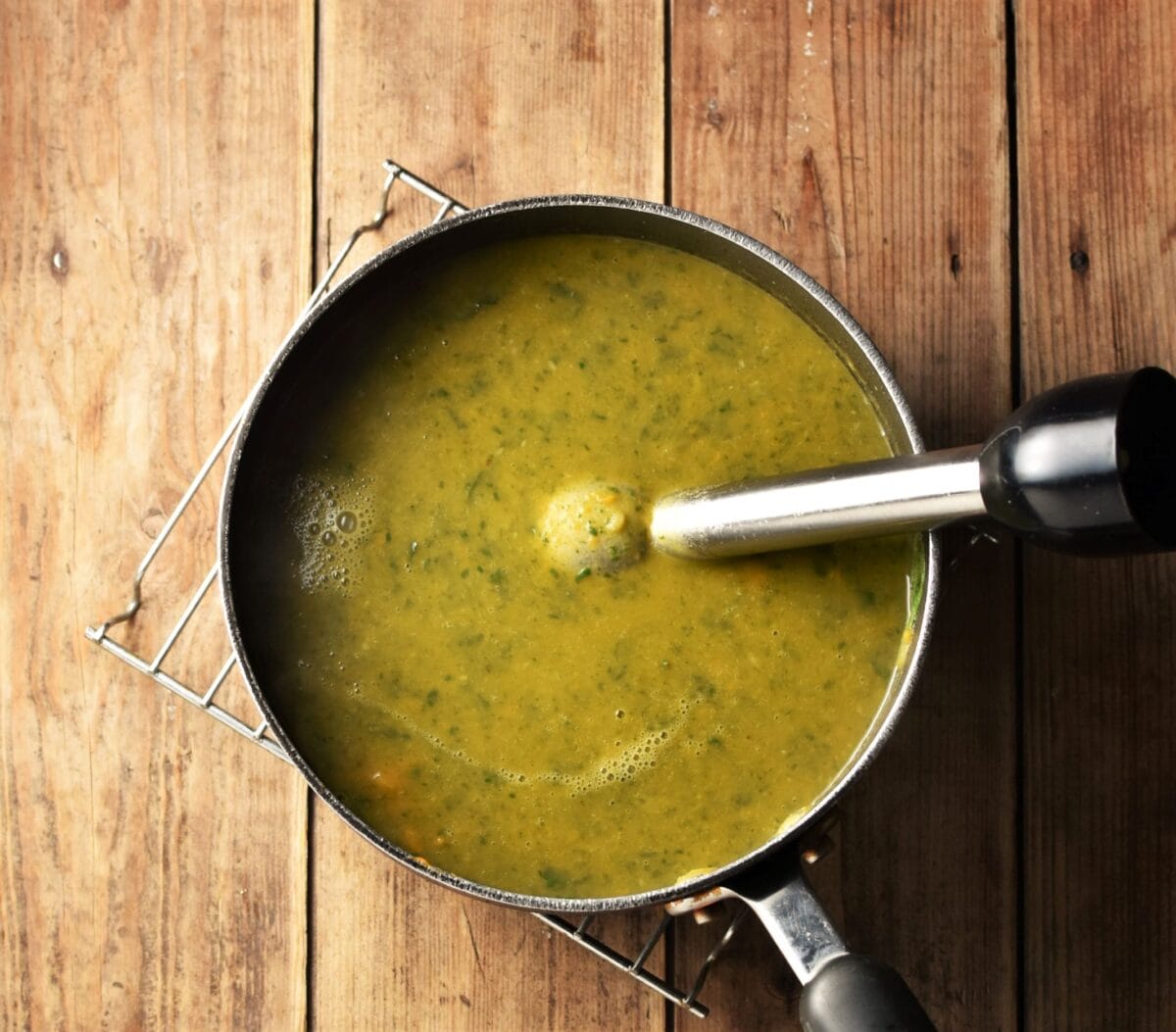 Puree green sweet potato soup in large pot with blender stick end piece on top of rack.