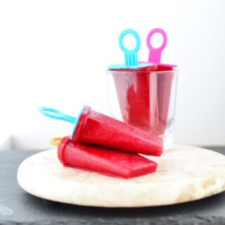 Side view of rooibos raspberry ice pops on top of marble plate and inside glass.