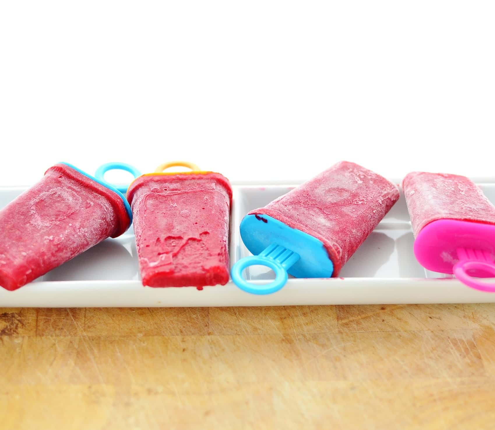 Rooibos raspberry ice lollies on top of white long dish, on wooden table.
