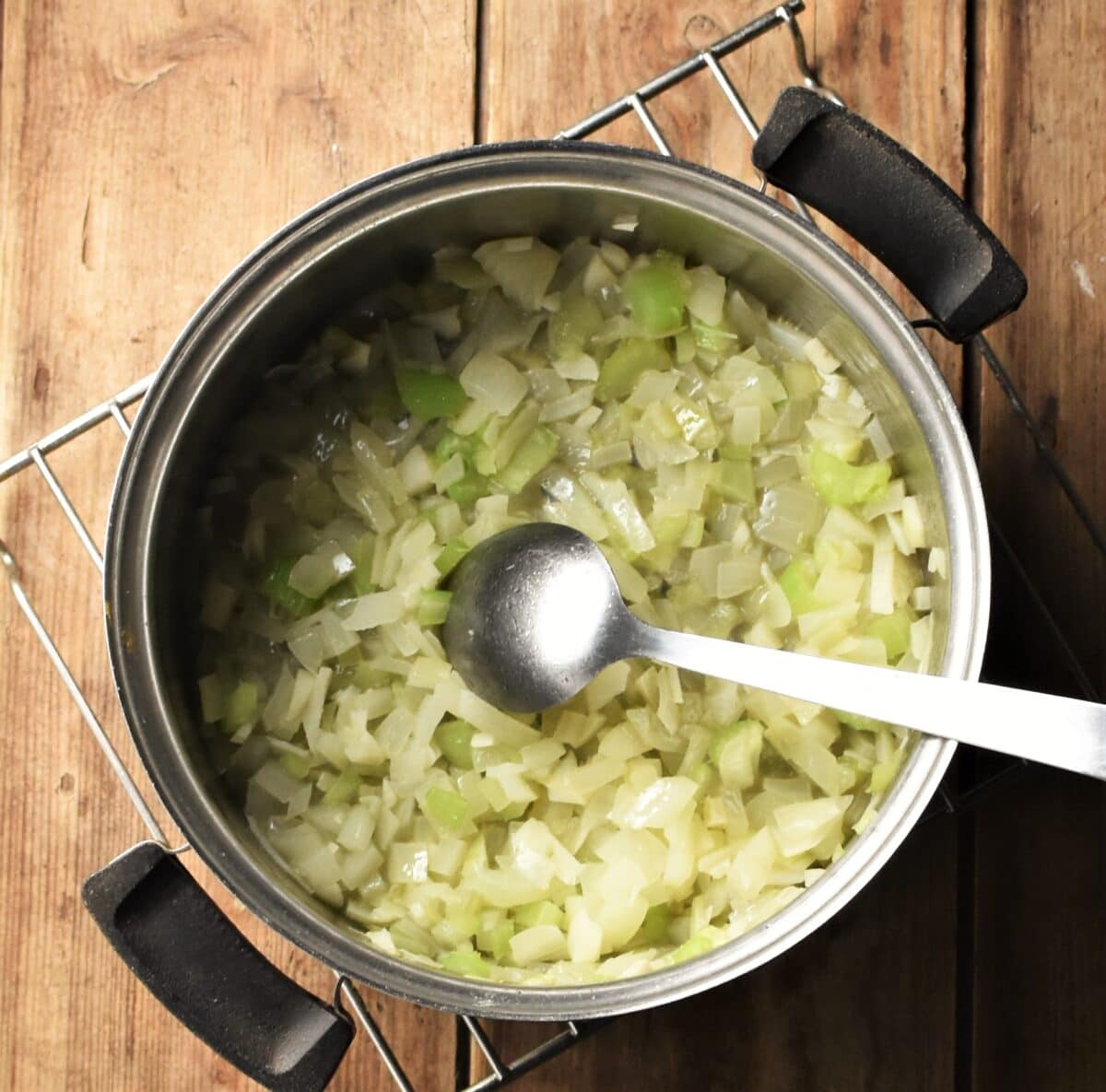 Chopped onion and celery in pot with spoon.