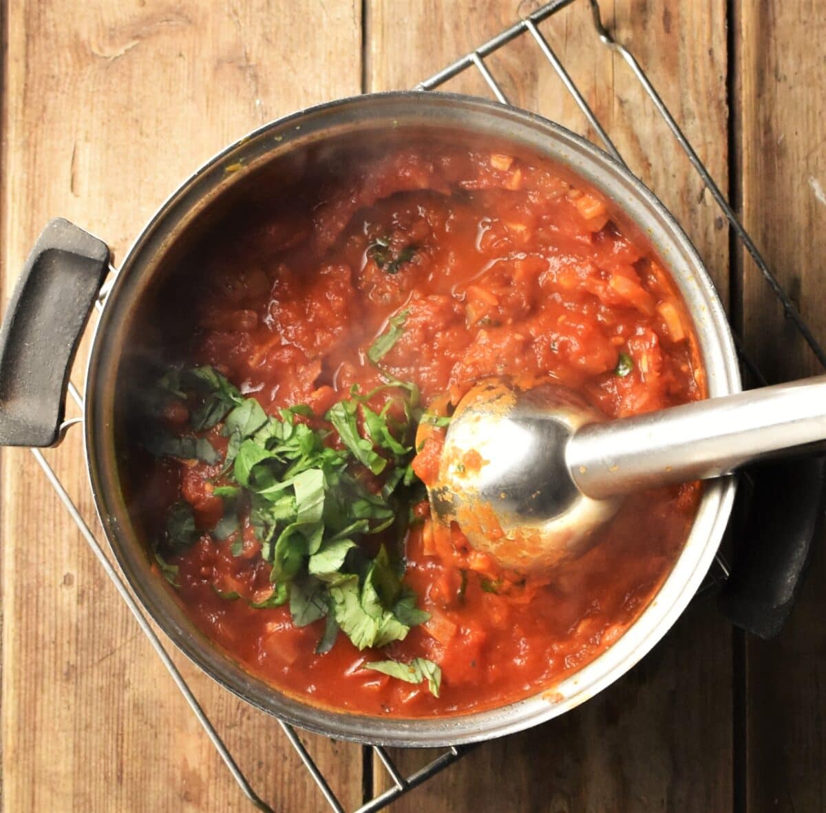 Tomato sauce with chopped basil and stick blender end piece in pot.