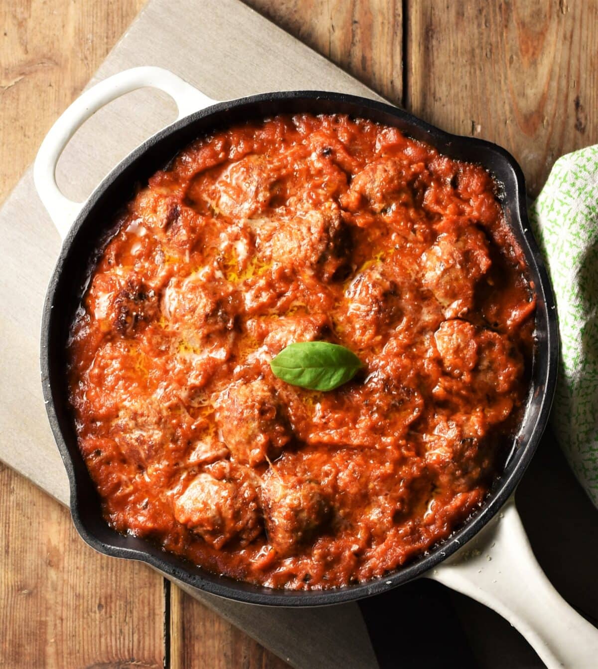 Meatballs in tomato sauce in pan on top of grey wooden board.