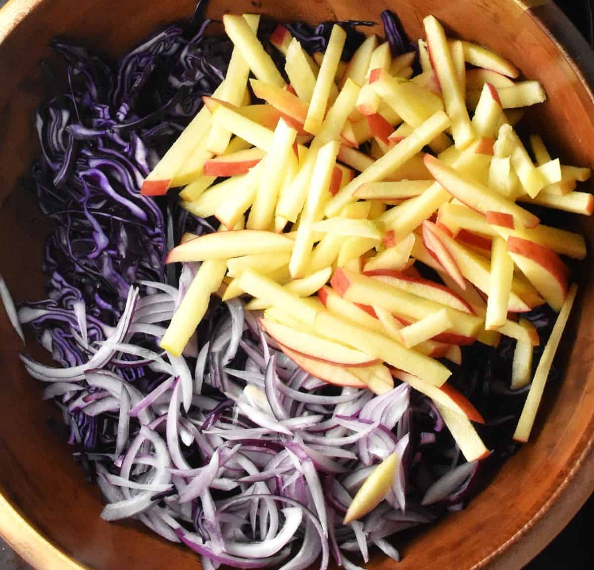 Apple matchsticks, shredded red cabbage and sliced red onion in wooden bowl.