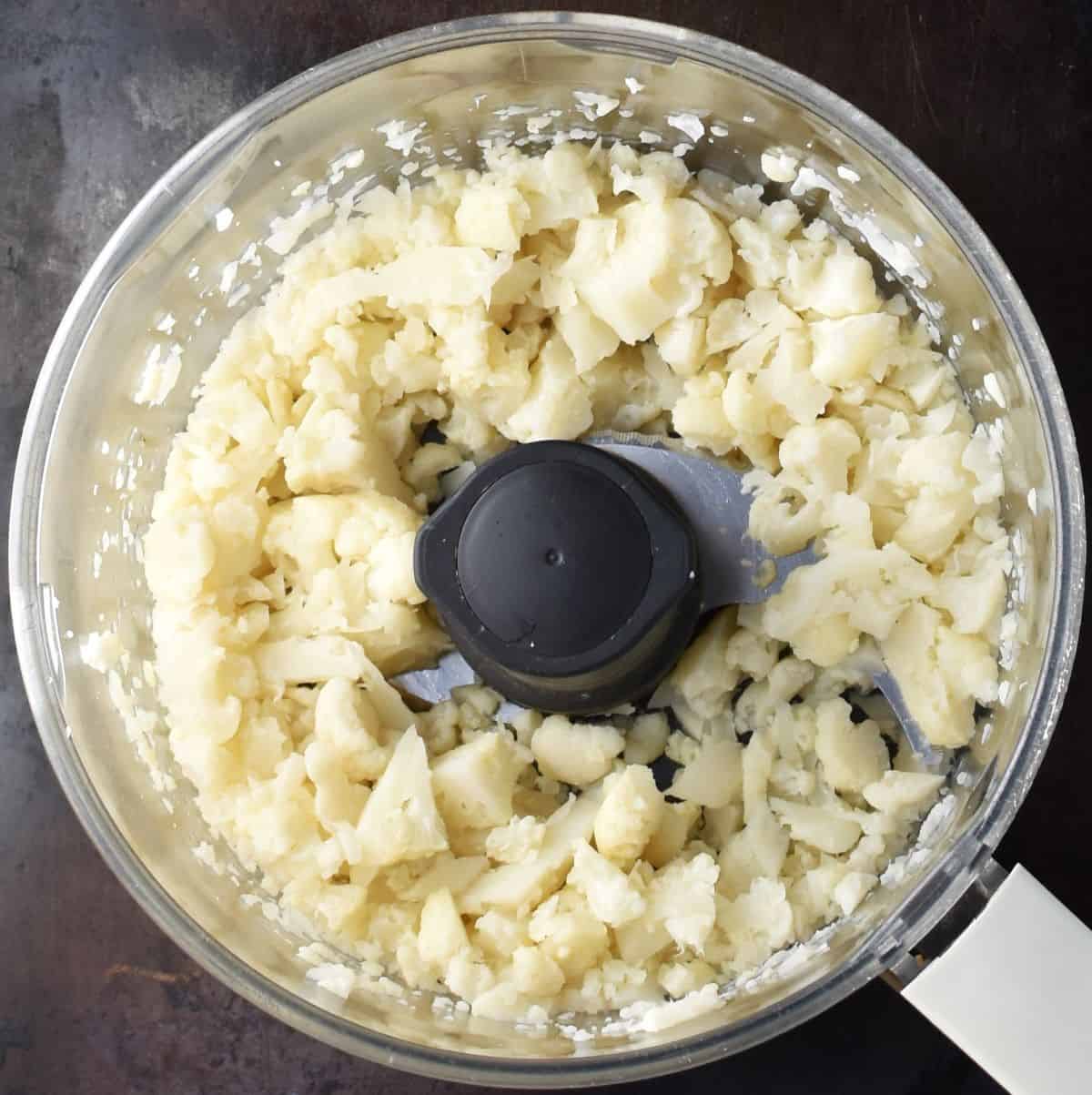 Pieces of cauliflower in food processor bowl.