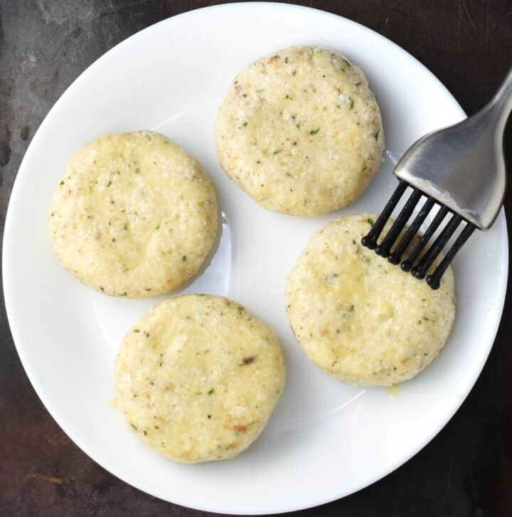 Brushing 4 cauliflower patties with egg wash on plate.