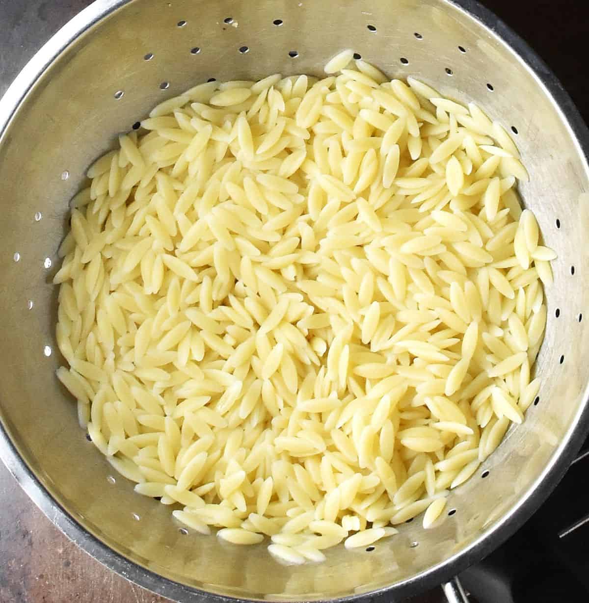 Cooked orzo pasta in metal strainer.