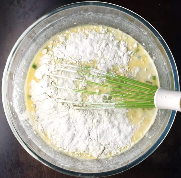 Egg quinoa muffin batter with flour on top on bowl with whisk.