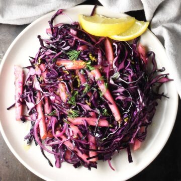 Top down view of red cabbage apple slaw with lemon wedges on pink plate.