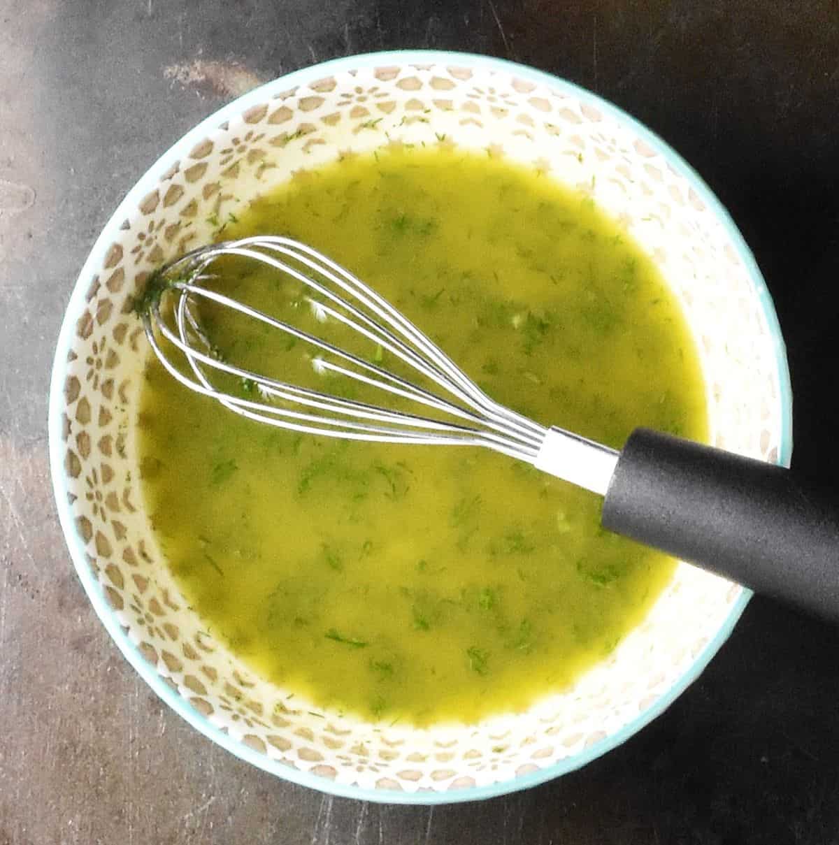 Salad dressing mixture with dill in grey bowl with small whisk.