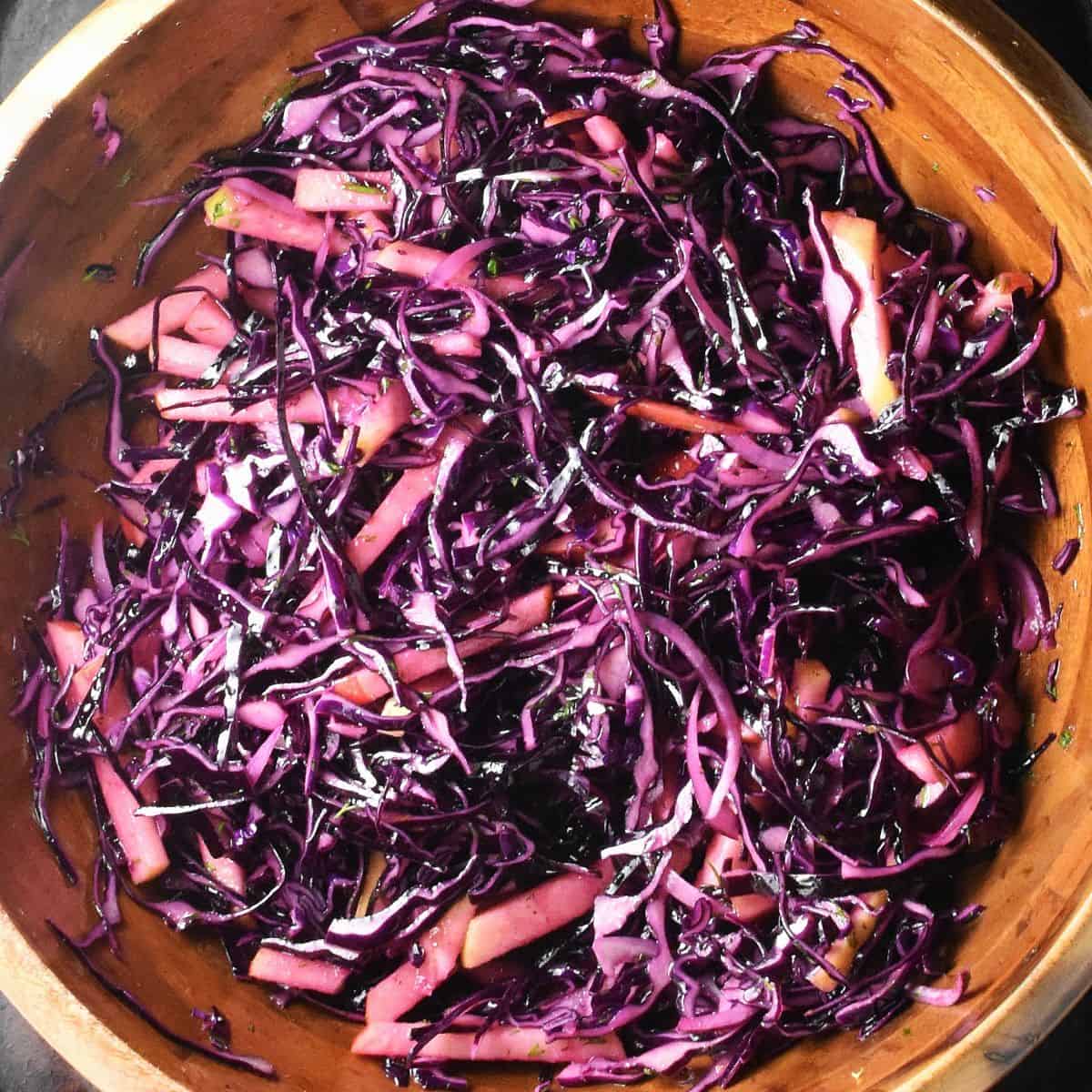 Top down view of red cabbage and apple slaw mixture in large wooden bowl.